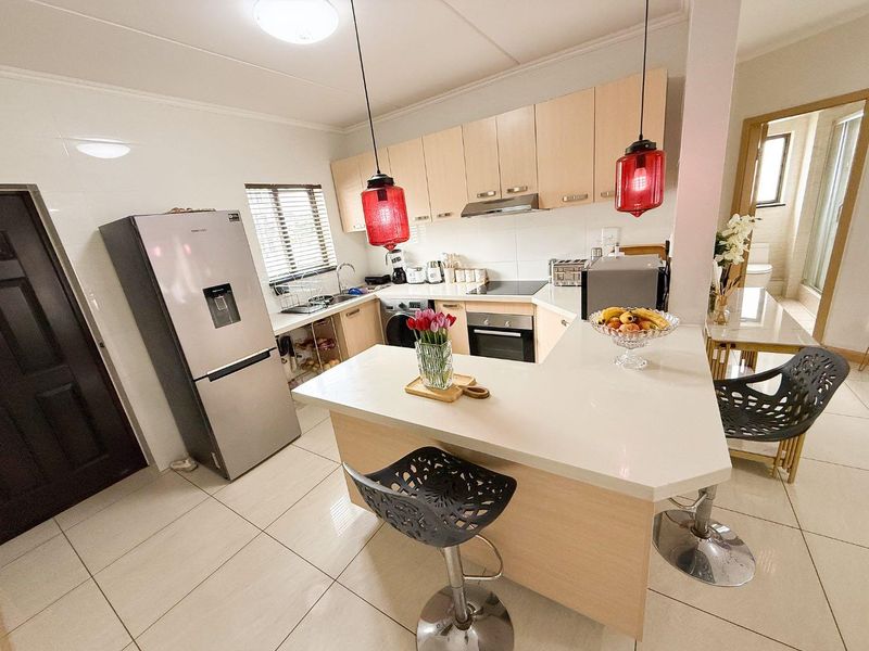 Modern kitchen featuring light wood cabinetry, stone countertops, a breakfast bar, and integrated appliances, finished with neutral floor tiles.