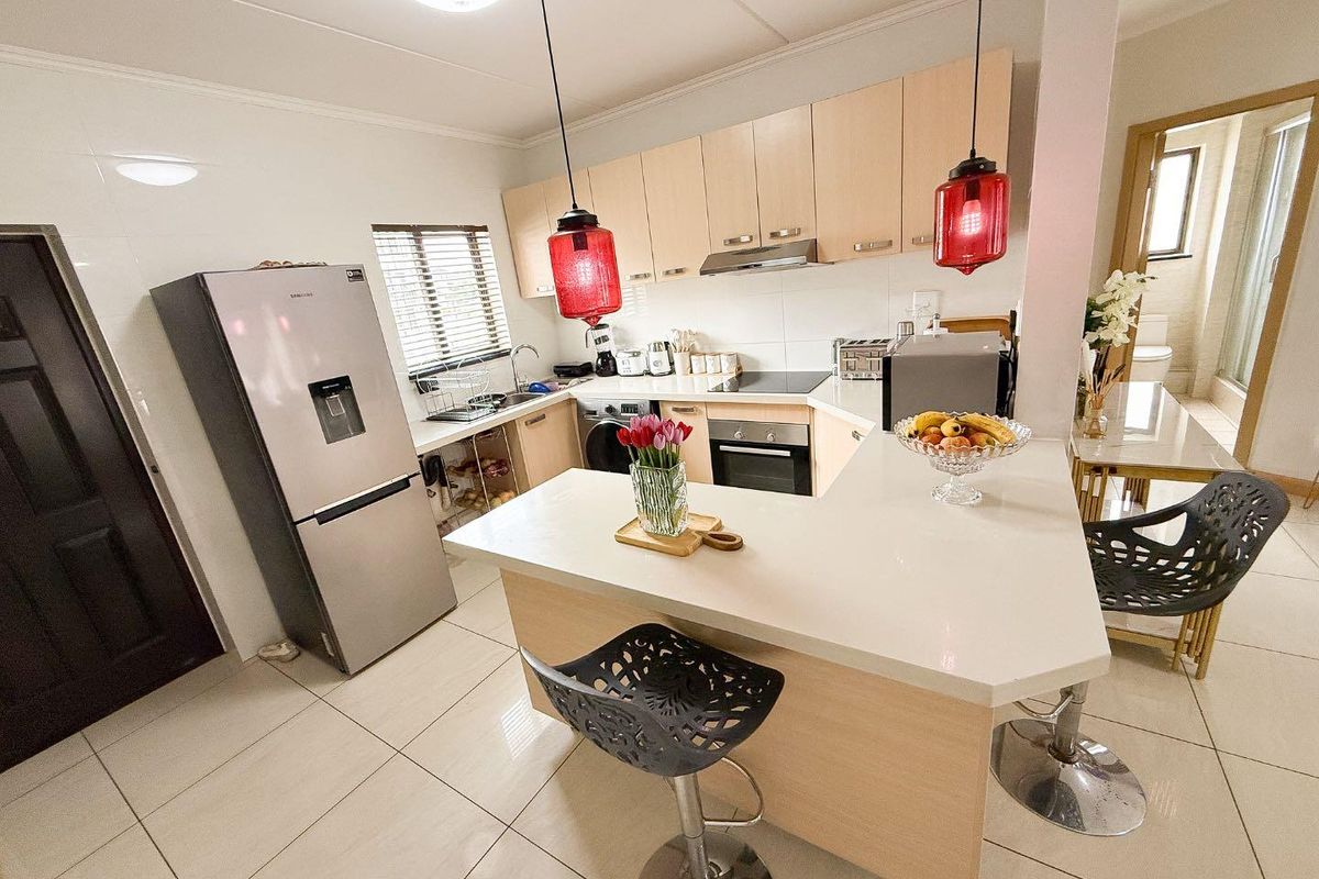 Modern kitchen featuring light wood cabinetry, stone countertops, a breakfast bar, and integrated appliances, finished with neutral floor tiles.