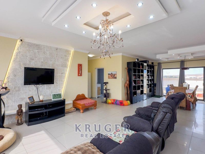 Spacious open-plan living and dining area featuring a stone accent wall, recessed ceiling with integrated lighting, and large format floor tiles.