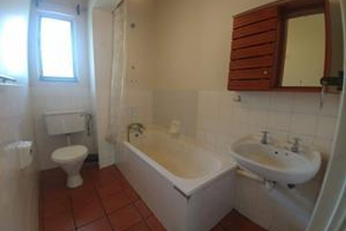 A functional bathroom featuring a bathtub, wall-mounted basin, and toilet with tiled flooring and wall finishes.