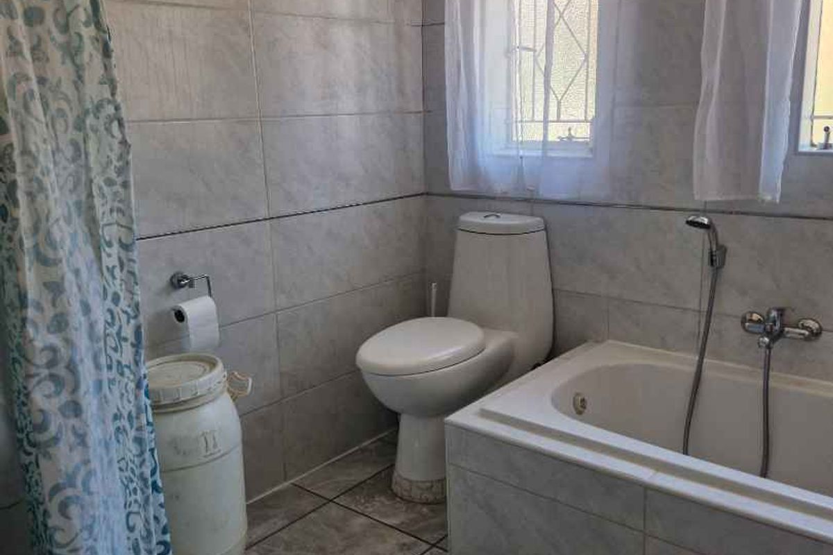 A functional bathroom featuring floor-to-ceiling wall tiles, a built-in bathtub with shower mixer, and a standard toilet.