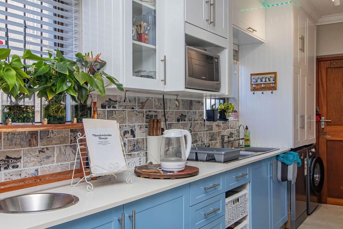 A well-maintained kitchen featuring blue lower cabinetry, white upper cabinets, stone countertops, a built-in microwave, and a decorative tiled backsplash.