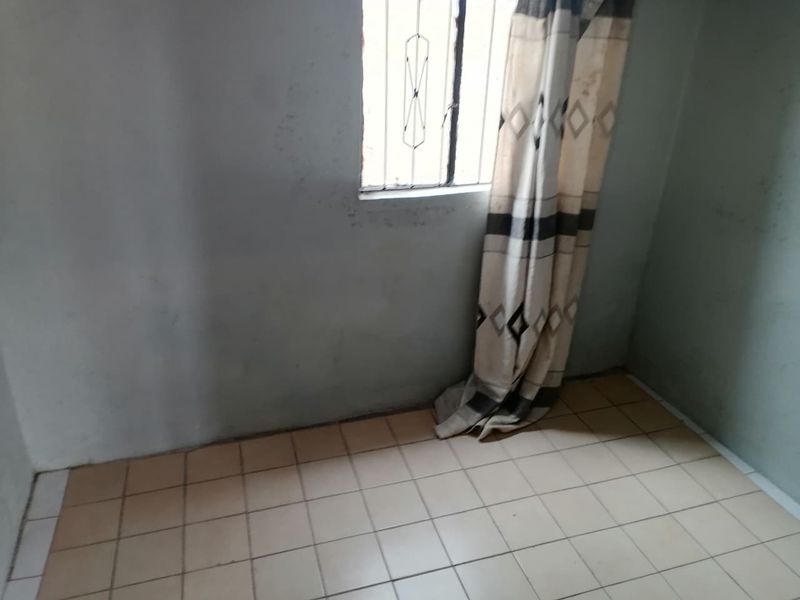 An empty bedroom featuring ceramic floor tiles and a window with security bars, requiring cosmetic updates to the wall finishes.