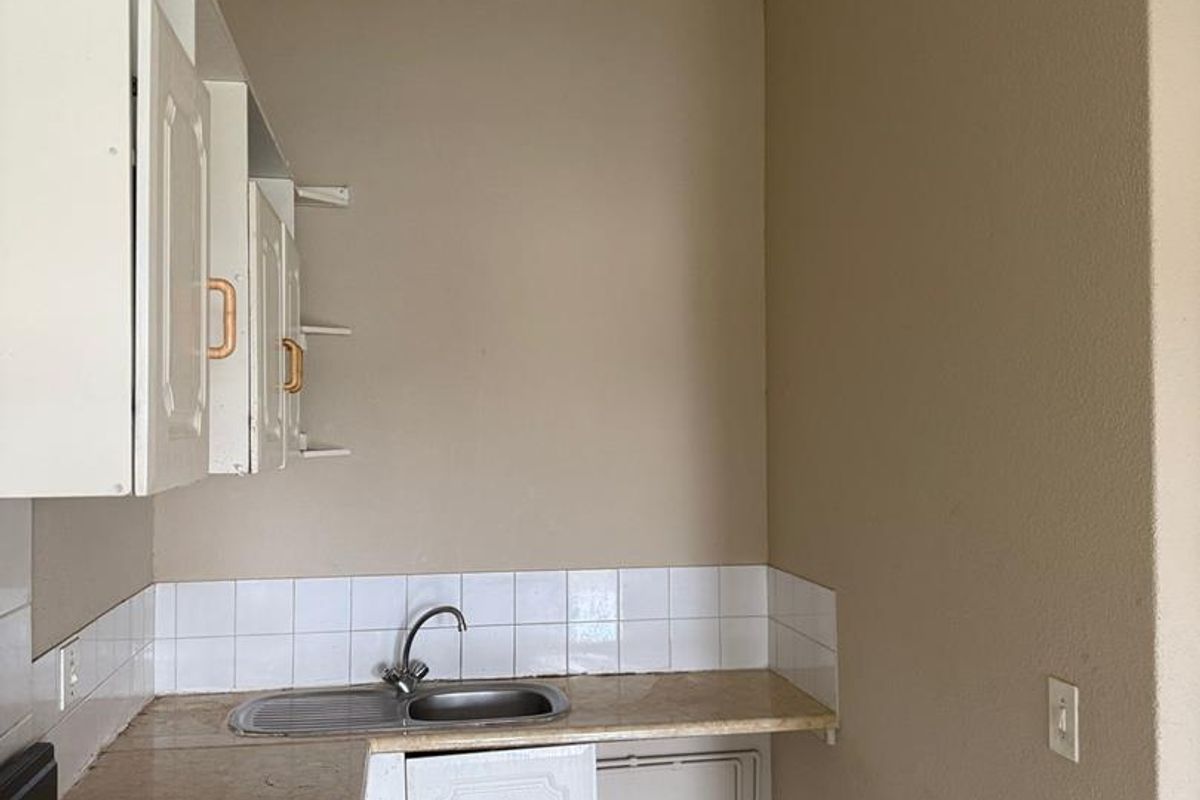 A compact kitchen area featuring basic cabinetry, a stainless steel sink, tiled backsplash, and a built-in electric stove.