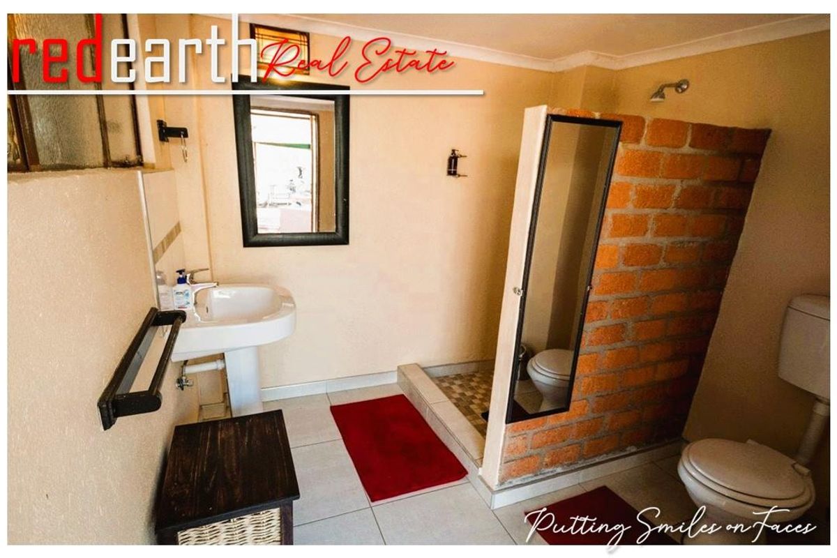 A functional bathroom featuring a pedestal basin, a toilet, and a walk-in shower area with an exposed brick partition wall.