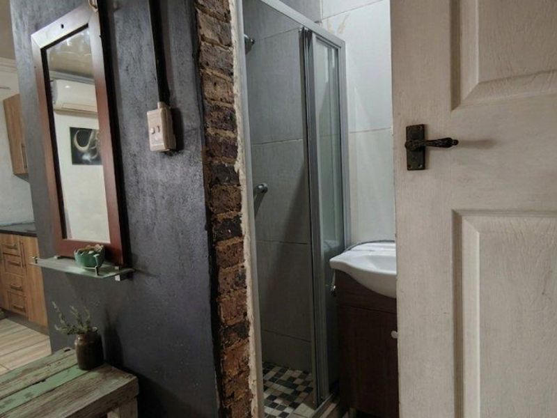 A small bathroom featuring a shower enclosure and vanity unit, currently showing unfinished wall edges and exposed brickwork around the entrance.
