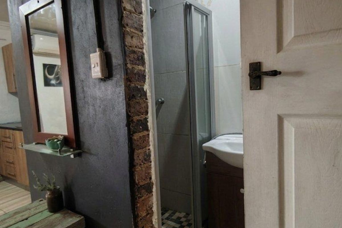 A small bathroom featuring a shower enclosure and vanity unit, currently showing unfinished wall edges and exposed brickwork around the entrance.