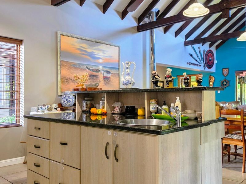 Spacious open-plan living area featuring a central kitchen island with granite countertops, exposed timber ceiling beams, and tiled flooring throughout.