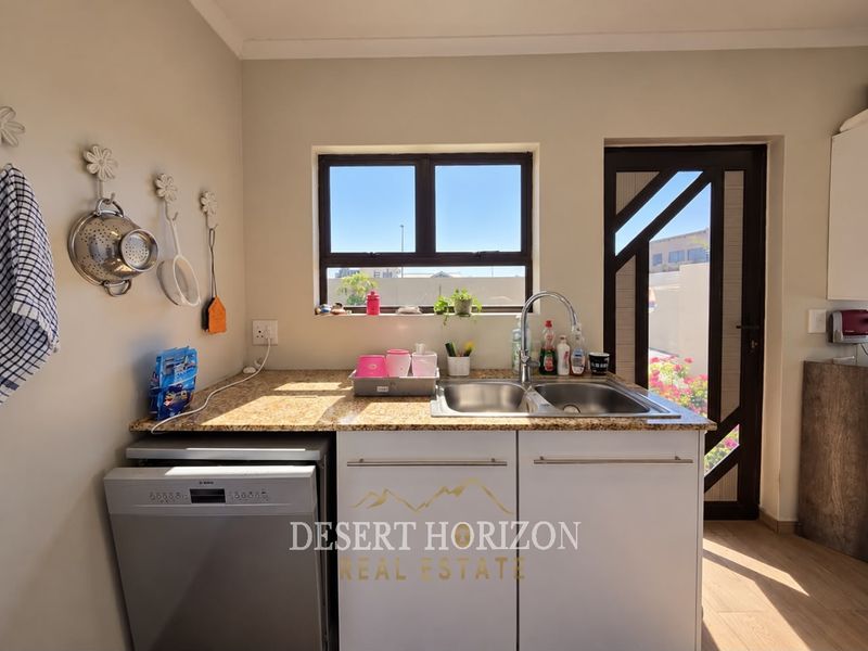 A functional scullery area featuring a double bowl sink, granite countertops, built-in cabinetry, and a dishwasher, with direct access to the exterior.