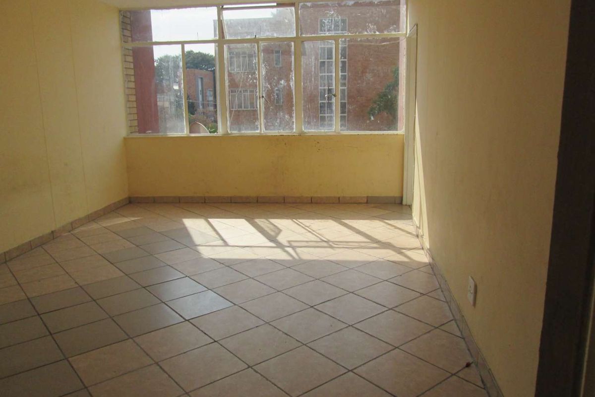 An empty, sunlit living area featuring tiled flooring and large windows, offering a blank canvas for renovation and interior design updates.