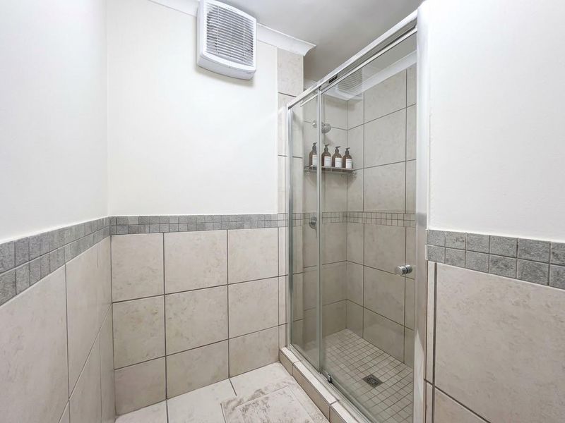 A clean, functional bathroom featuring a tiled shower enclosure with a sliding glass door and a wall-mounted extractor fan.