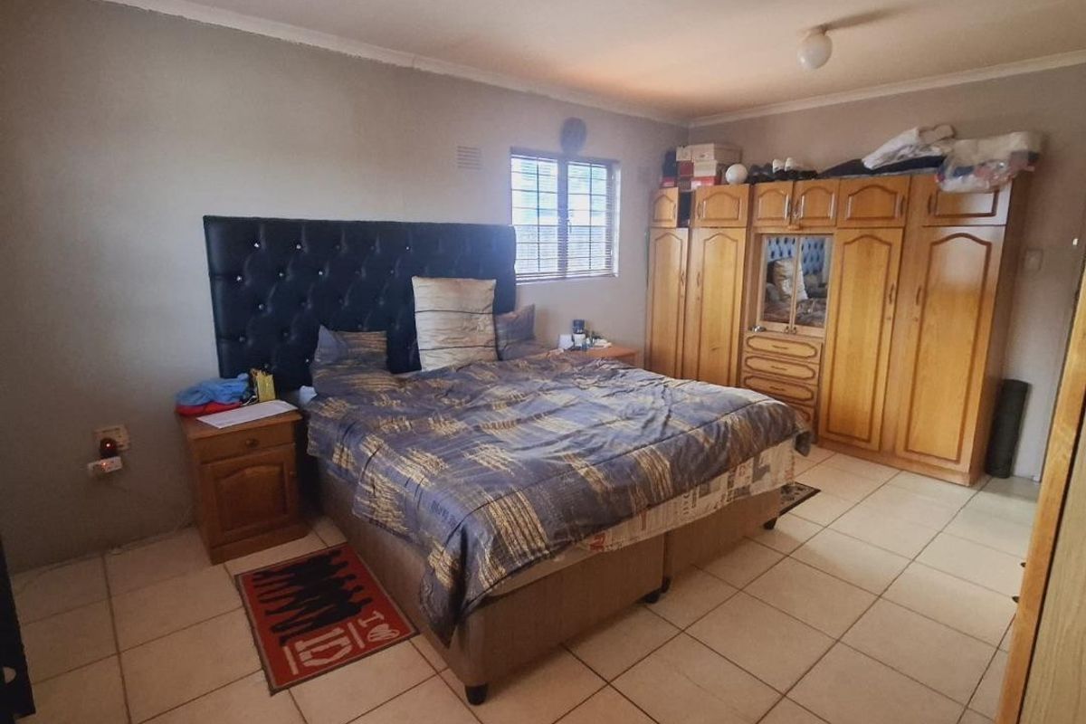 A bedroom featuring tiled flooring, built-in wooden cupboards, and a window providing natural light.