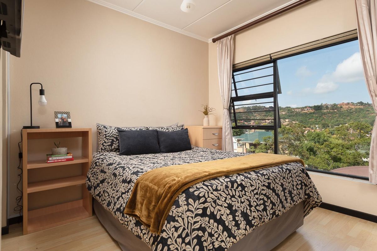 A well-lit bedroom featuring light-toned laminate flooring, neutral wall finishes, and a large window offering scenic hillside views.