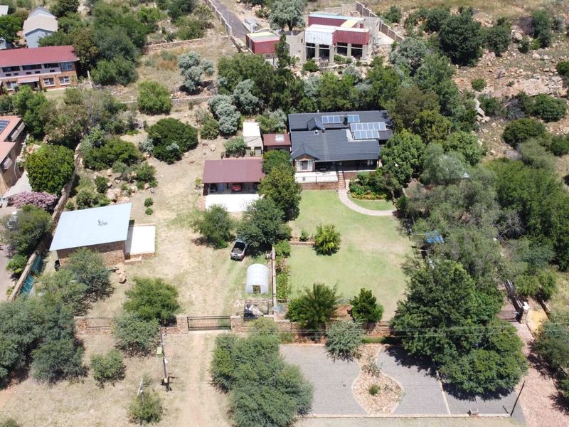 Aerial view of a residential property featuring a main house with solar panels, a detached garage, expansive garden, and paved driveway access.