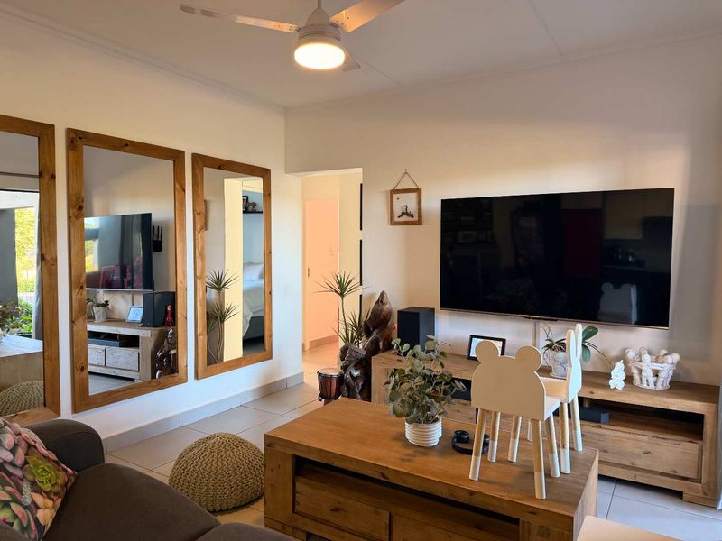 A well-maintained living room featuring tiled flooring, a ceiling fan, and large wall-mounted mirrors, creating a bright and functional living space.