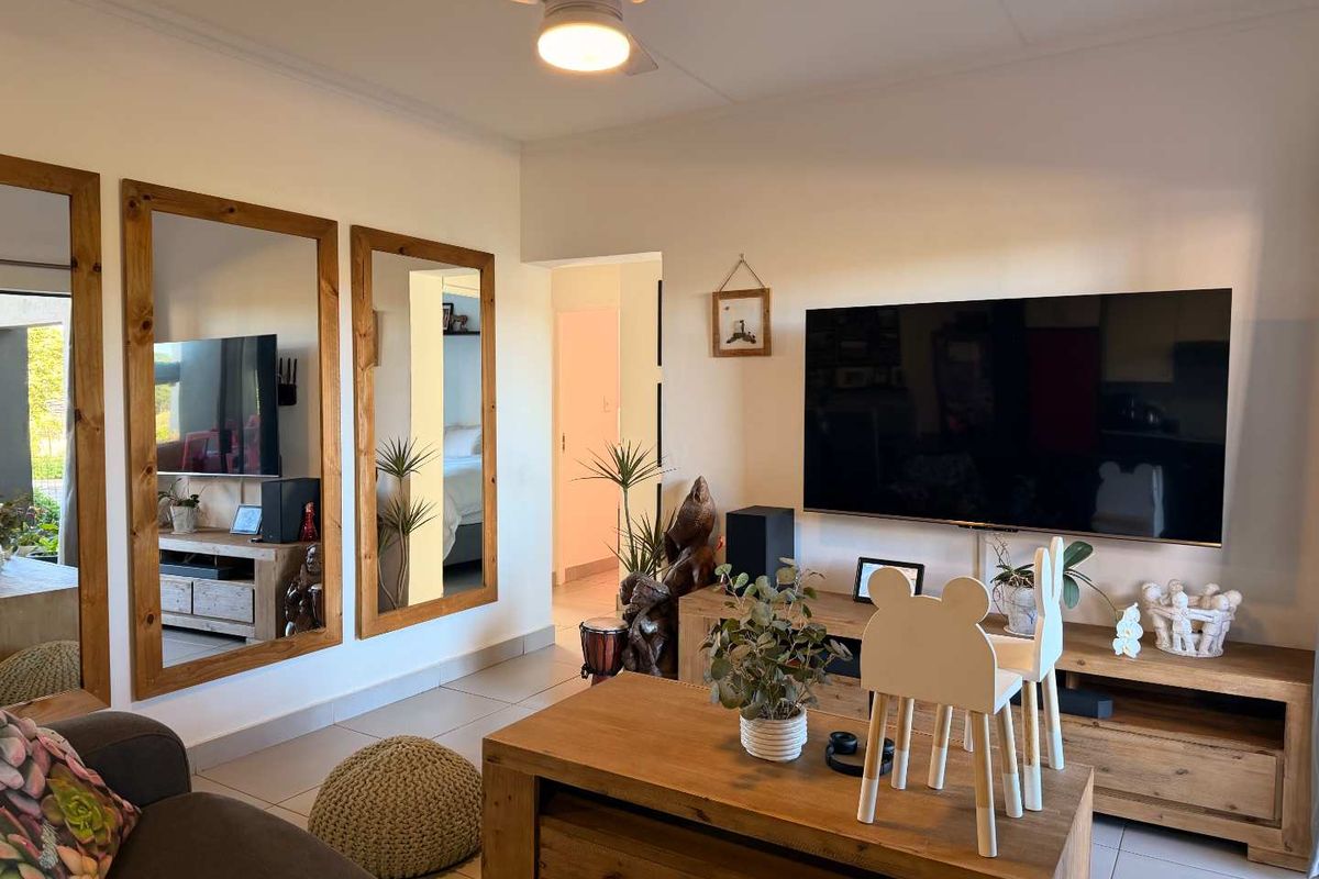 A well-maintained living room featuring tiled flooring, a ceiling fan, and large wall-mounted mirrors, creating a bright and functional living space.