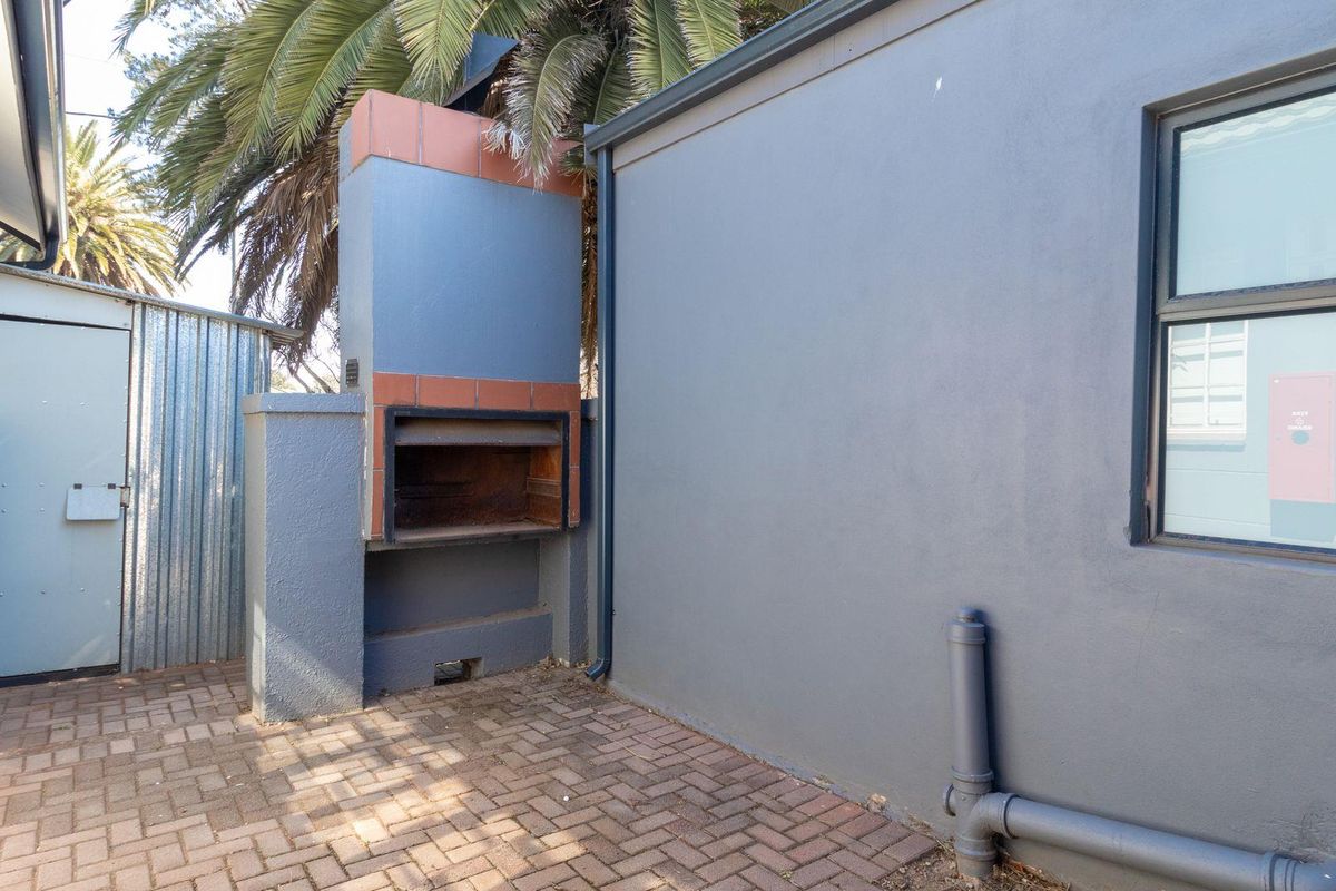 An outdoor paved area featuring a built-in brick fireplace and a corrugated metal storage shed attached to the office building exterior.