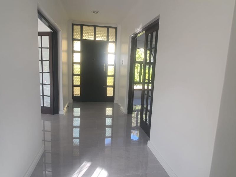 A bright and spacious hallway featuring polished tiled flooring, recessed lighting, and elegant dark-framed french doors leading to adjacent rooms.
