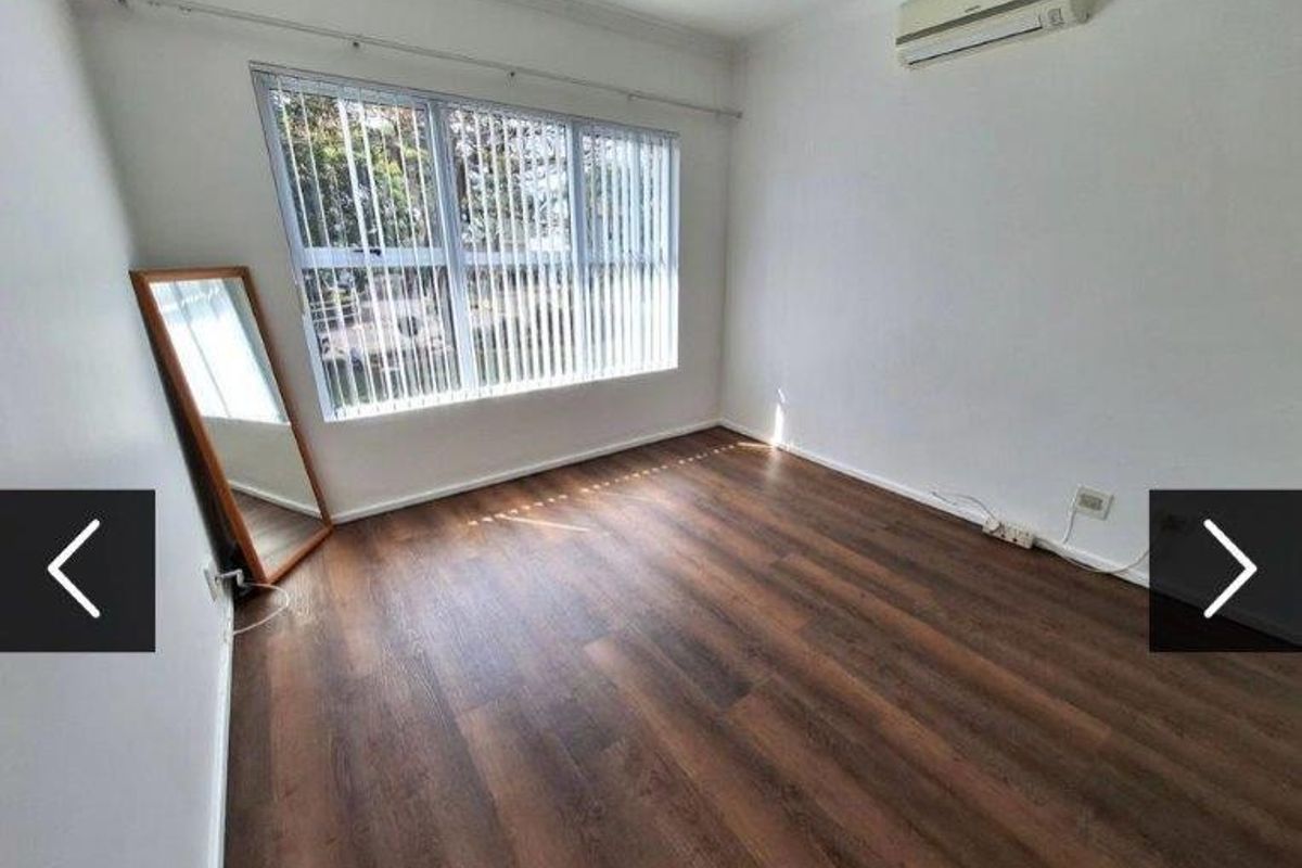 A bright, empty bedroom featuring dark laminate flooring, vertical window blinds, and a wall-mounted split-system air conditioning unit.