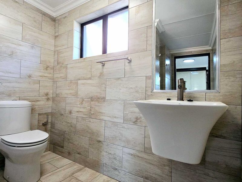 A modern, well-maintained bathroom featuring wood-look tiled walls, a wall-mounted basin, and a clean, minimalist aesthetic.
