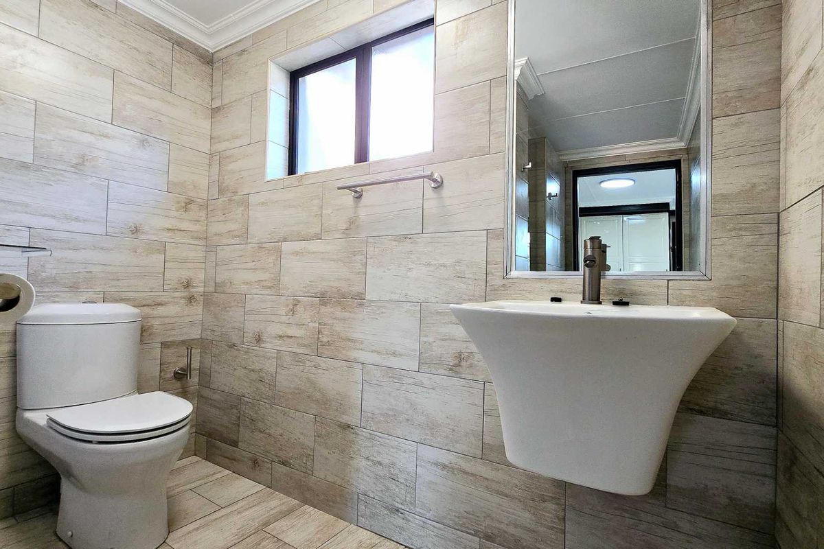 A modern, well-maintained bathroom featuring wood-look tiled walls, a wall-mounted basin, and a clean, minimalist aesthetic.