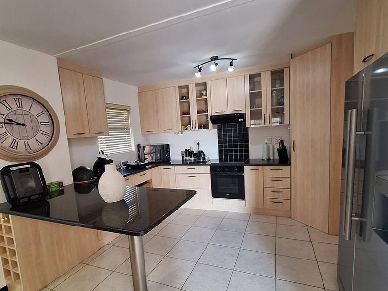 A functional kitchen featuring light wood cabinetry, black granite countertops, a breakfast bar, and tiled flooring with integrated oven and extractor fan.