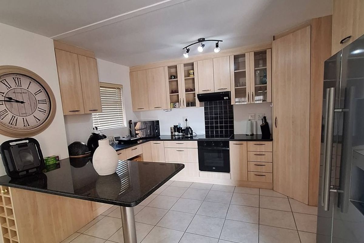 A functional kitchen featuring light wood cabinetry, black granite countertops, a breakfast bar, and tiled flooring with integrated oven and extractor fan.