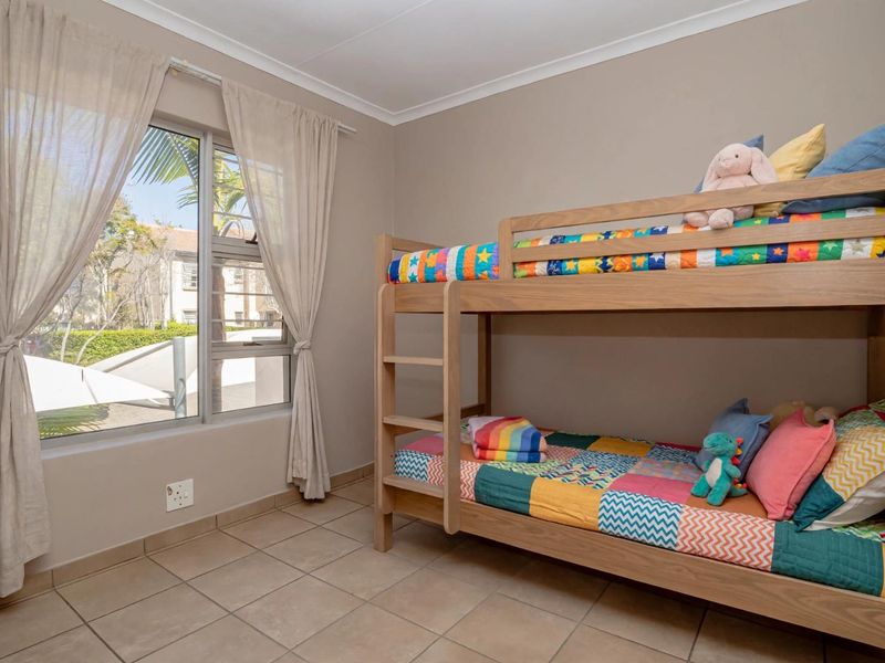 A well-maintained bedroom featuring neutral wall tones, tiled flooring, and a large window providing natural light.