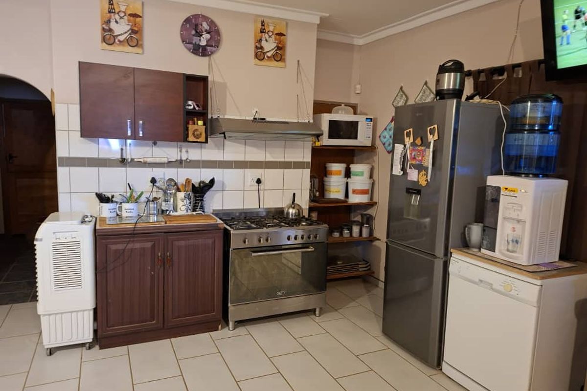 Functional kitchen featuring dark wood cabinetry, a stainless steel freestanding stove with extractor fan, tiled flooring, and a tiled backsplash.