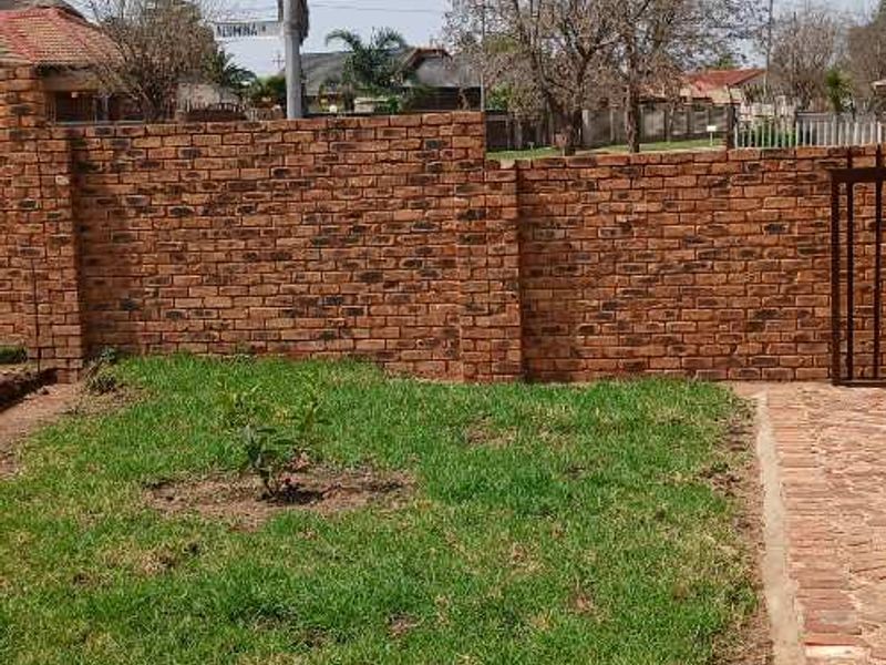A private rear garden area featuring a face brick boundary wall, a small lawn, and brick paved pathways.