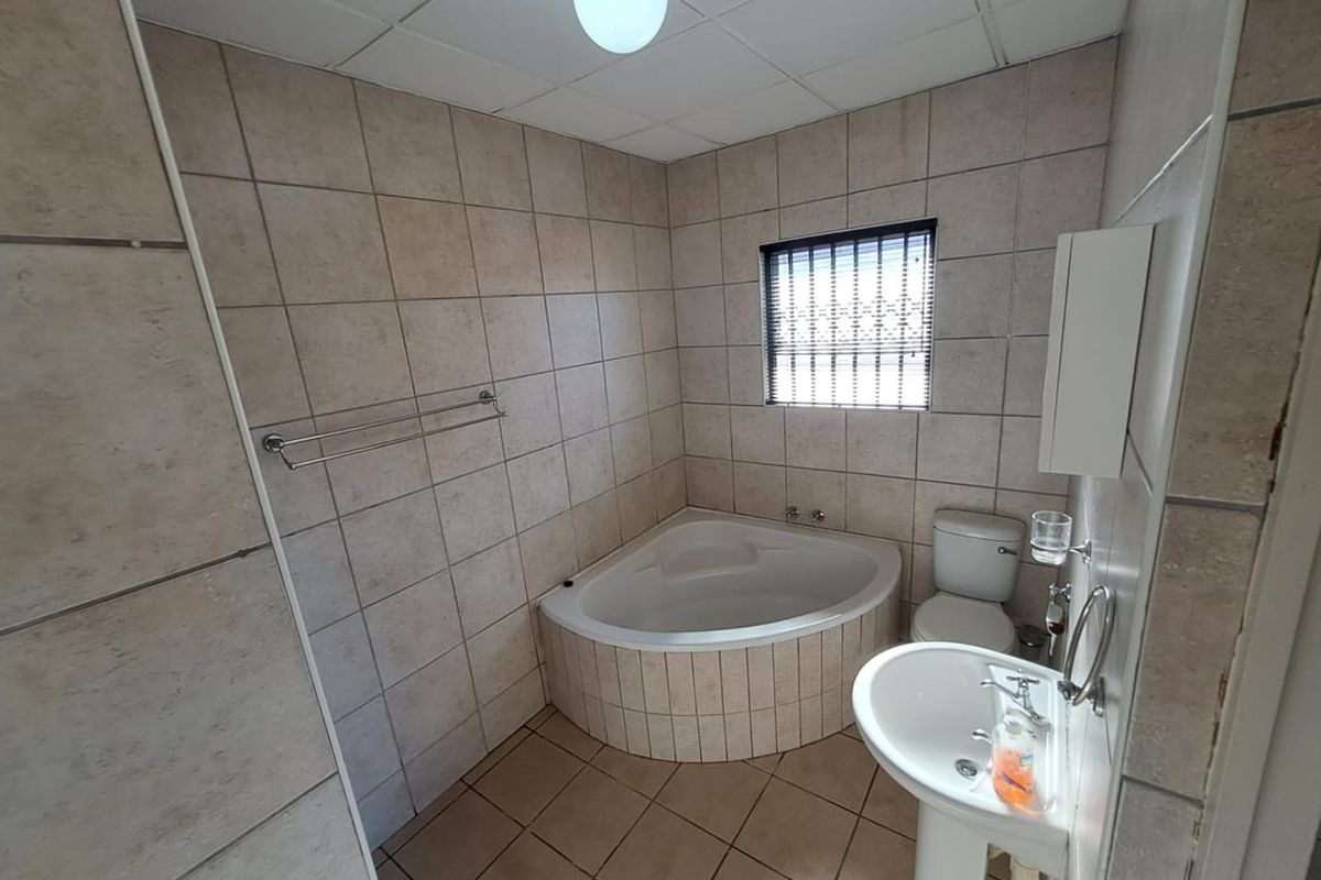 A functional bathroom featuring a corner bathtub, pedestal basin, and toilet, finished with neutral wall and floor tiling.