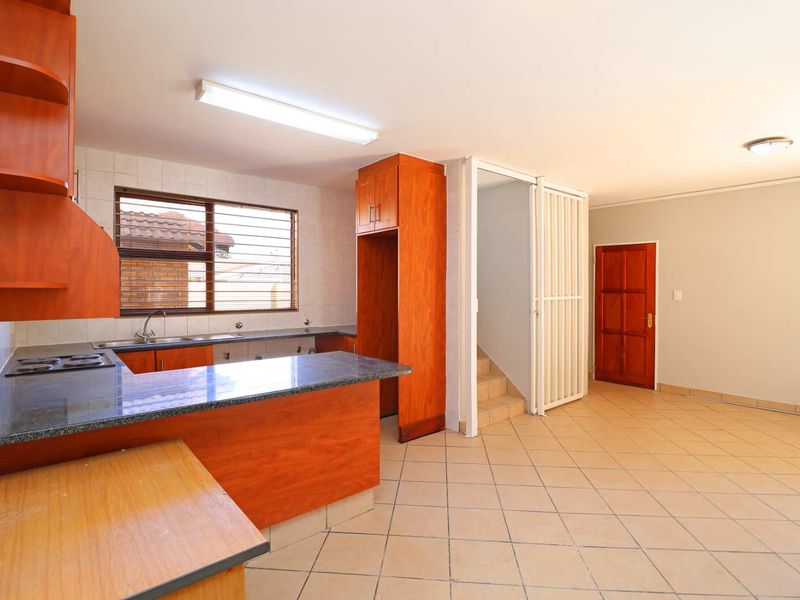 Open-plan kitchen and living area featuring wooden cabinetry, granite countertops, tiled flooring, and direct access to the staircase.