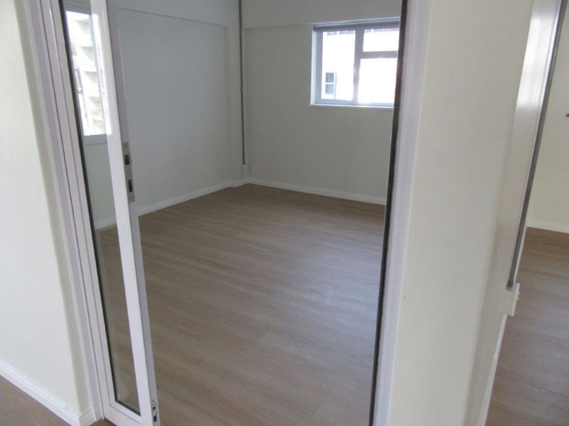 A bright, empty bedroom featuring modern laminate flooring, neutral walls, and sliding glass door access, providing a clean and versatile living space.
