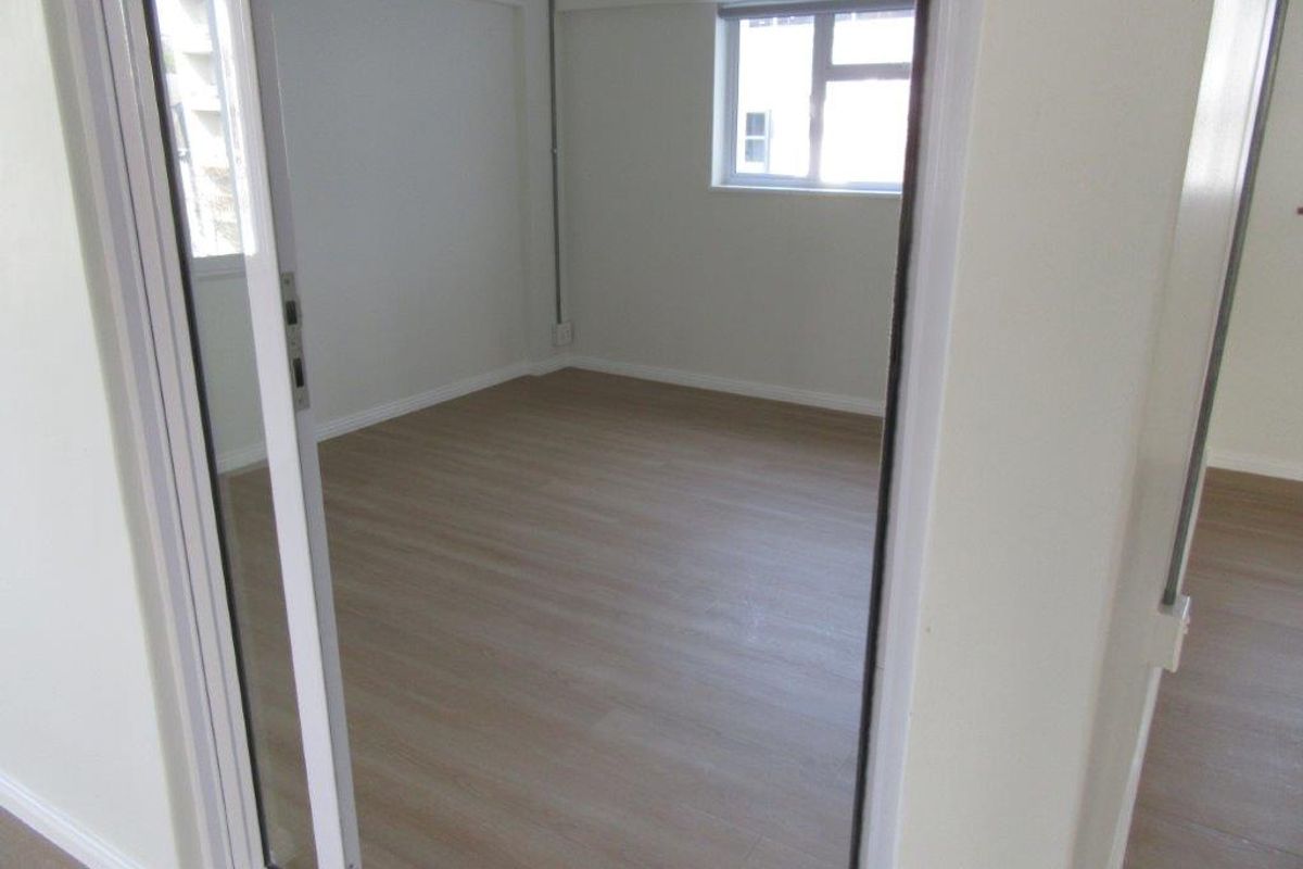 A bright, empty bedroom featuring modern laminate flooring, neutral walls, and sliding glass door access, providing a clean and versatile living space.