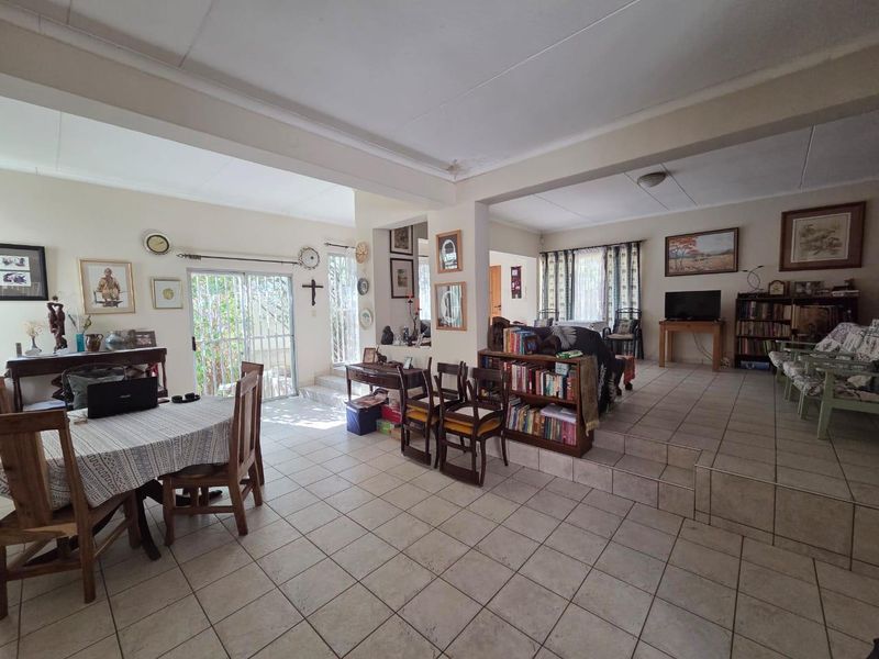 Spacious open-plan living and dining area featuring ceramic tile flooring, a stepped floor transition, and sliding glass doors with security gates.