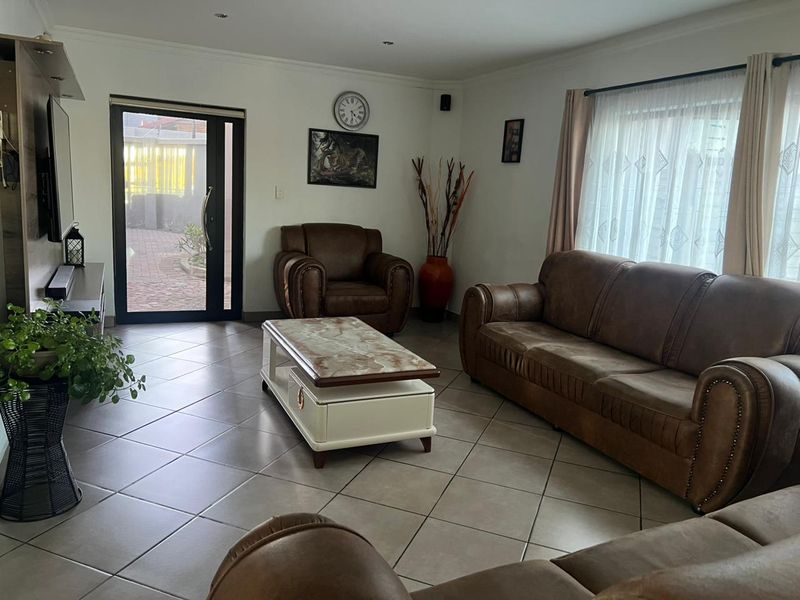A spacious living room featuring neutral tiled flooring, recessed downlighting, and a glass-panelled door providing direct access to the outdoor area.