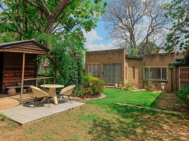 Rear garden view featuring a brick exterior, sliding glass doors with security bars, a paved patio area, and a detached wooden gazebo.