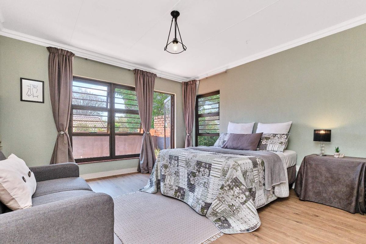 A well-lit bedroom featuring large windows with security bars, laminate flooring, and crown molding, offering a comfortable and functional living space.