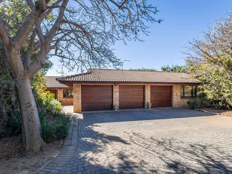 Front exterior view of the property featuring a triple garage with timber doors, brick facade, and a spacious circular paved driveway.