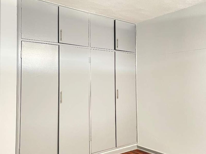 A vacant bedroom featuring classic parquet flooring and floor-to-ceiling built-in cupboards, offering a clean canvas for personalization.