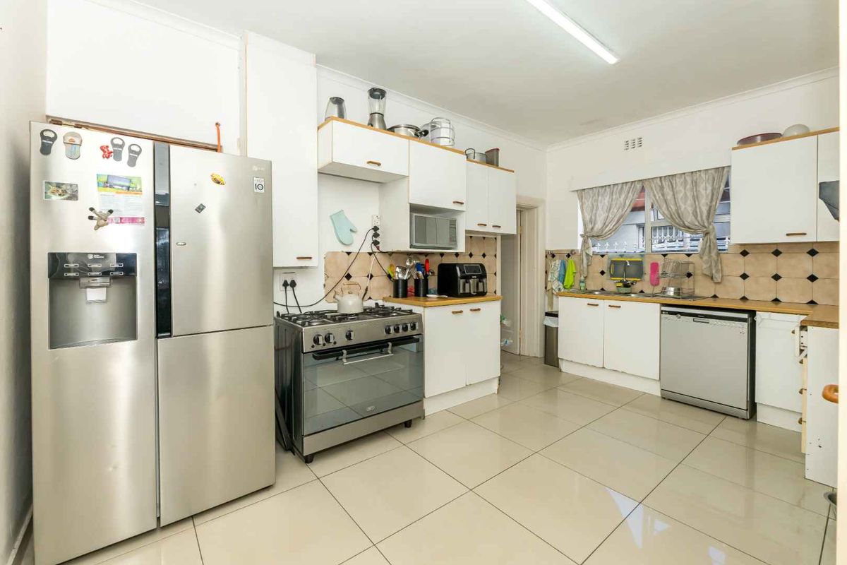 Functional kitchen featuring tiled flooring, white cabinetry, a gas stove with oven, and a double-basin sink with tiled backsplash.