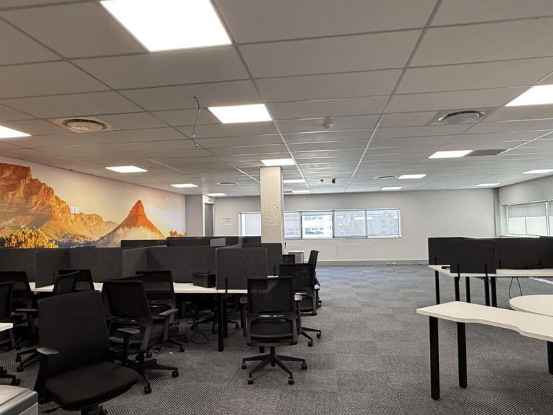 Open-plan office space featuring suspended ceilings with recessed lighting, carpeted flooring, and integrated desk workstations with privacy partitions.