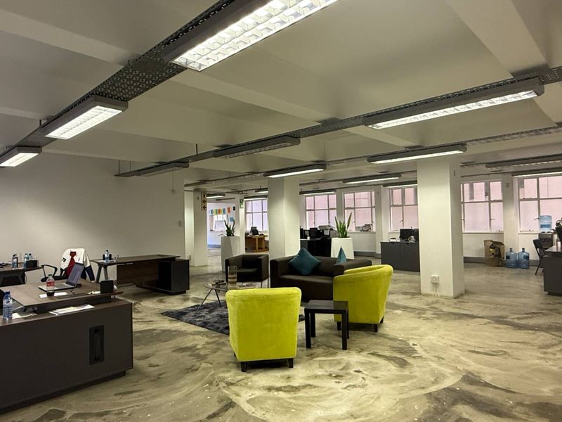 Open-plan office space featuring industrial-style exposed ceiling lighting, structural columns, and polished concrete flooring throughout the workspace.