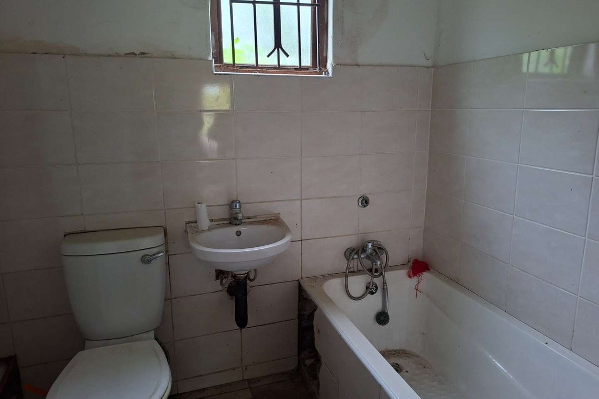 A dated bathroom featuring a standard bathtub, wall-mounted basin, and toilet, requiring significant renovation and cosmetic updates to improve its condition.
