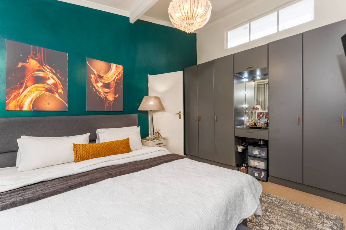 A well-appointed bedroom featuring built-in grey cabinetry with an integrated vanity station, high ceilings, and a bold accent wall.