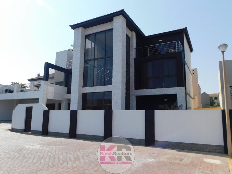 Modern multi-story residential property featuring striking stone cladding, expansive glass windows, a private balcony, and a secure boundary wall with a paved driveway.
