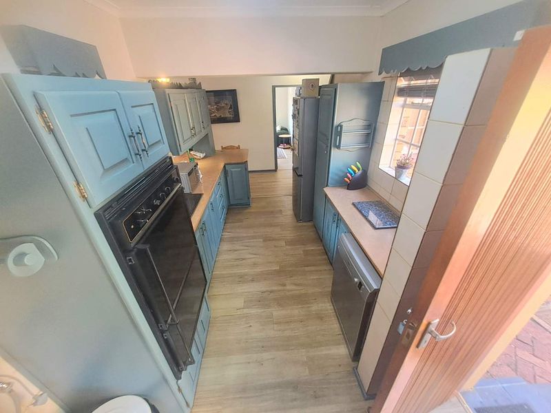 A galley-style kitchen featuring blue cabinetry, wood-look laminate flooring, and a built-in oven, offering a functional layout with potential for modern updates.