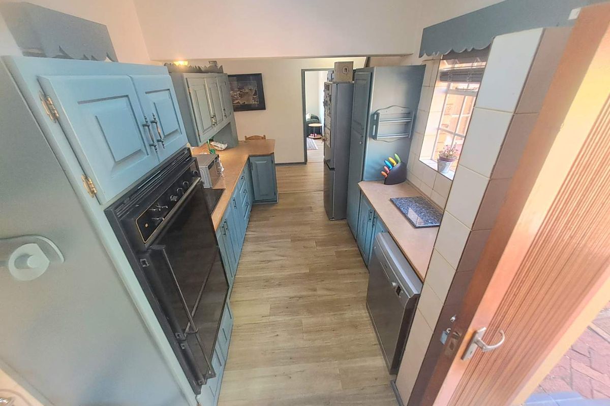 A galley-style kitchen featuring blue cabinetry, wood-look laminate flooring, and a built-in oven, offering a functional layout with potential for modern updates.