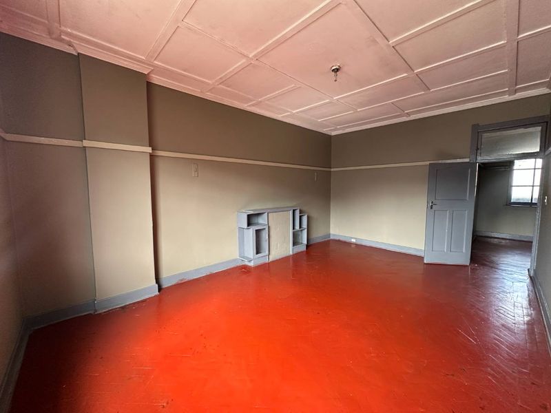 An empty living room featuring a coffered ceiling, built-in shelving, and painted timber flooring, offering a blank canvas for renovation.