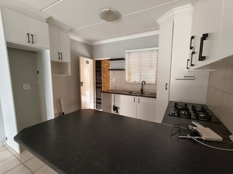 A functional kitchen featuring white cabinetry, a dark countertop, a gas hob, and a breakfast nook, with tiled flooring and neutral wall finishes.
